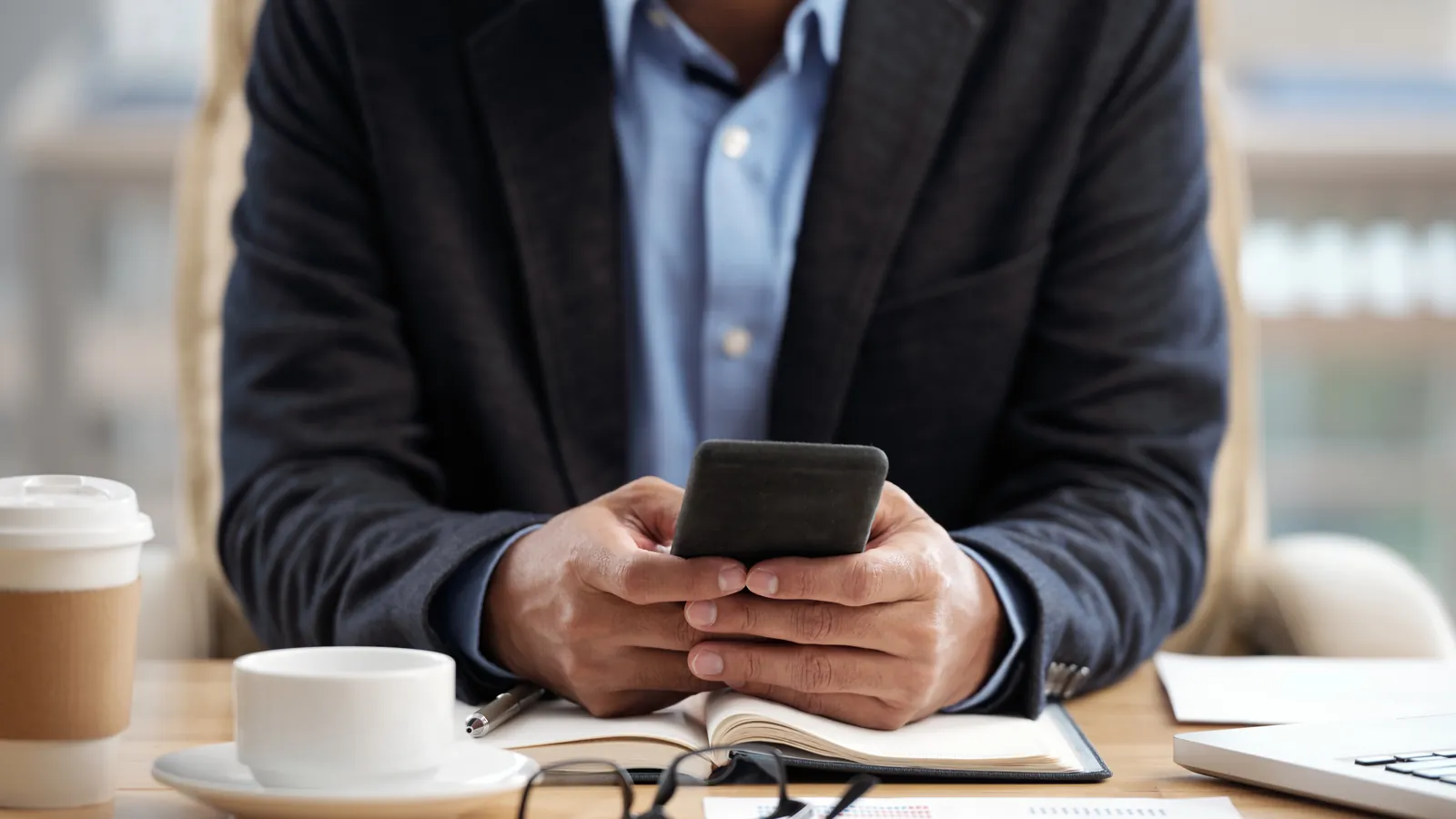Advogado de terno lendo mensagens no celular, com agenda aberta e café sobre a mesa