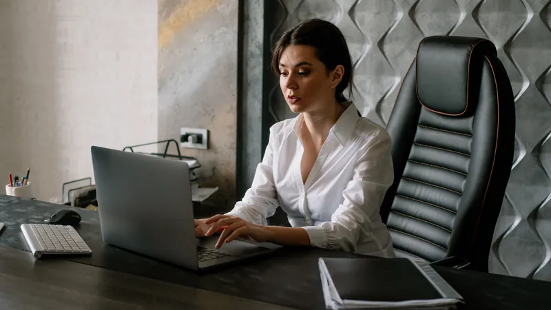 Advogada de camisa branca sentada à mesa do escritório, trabalhando no notebook